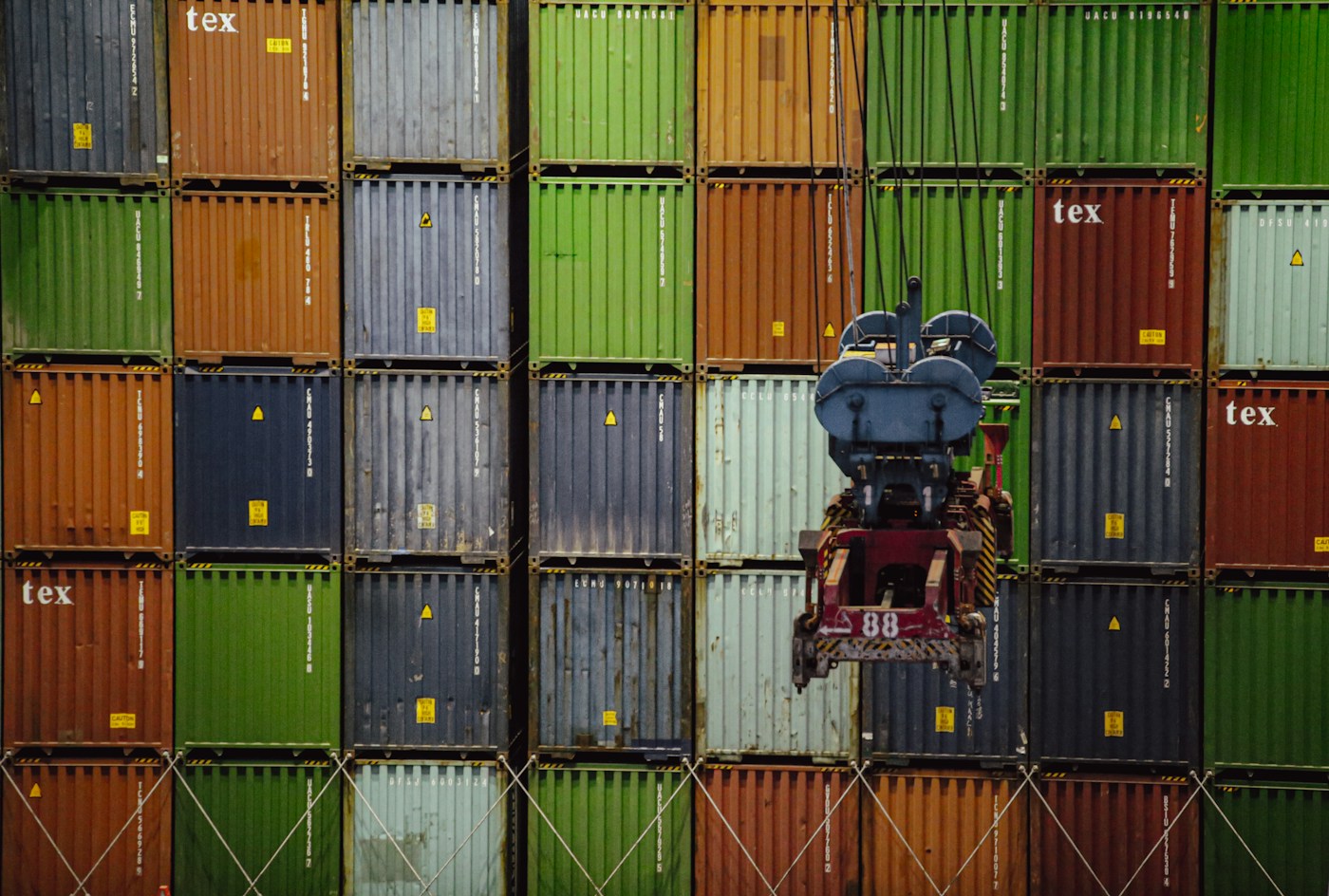 Container di diversi colori impilati dietro un dispositivo di sollevamento portuale